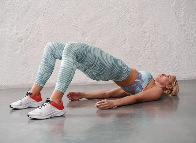 Young sporty woman in sportswear, leggings and bra practicing yoga, beautiful girl doing Glute Bridge exercise, dvi pada pithasana pose, working out in yoga studio.